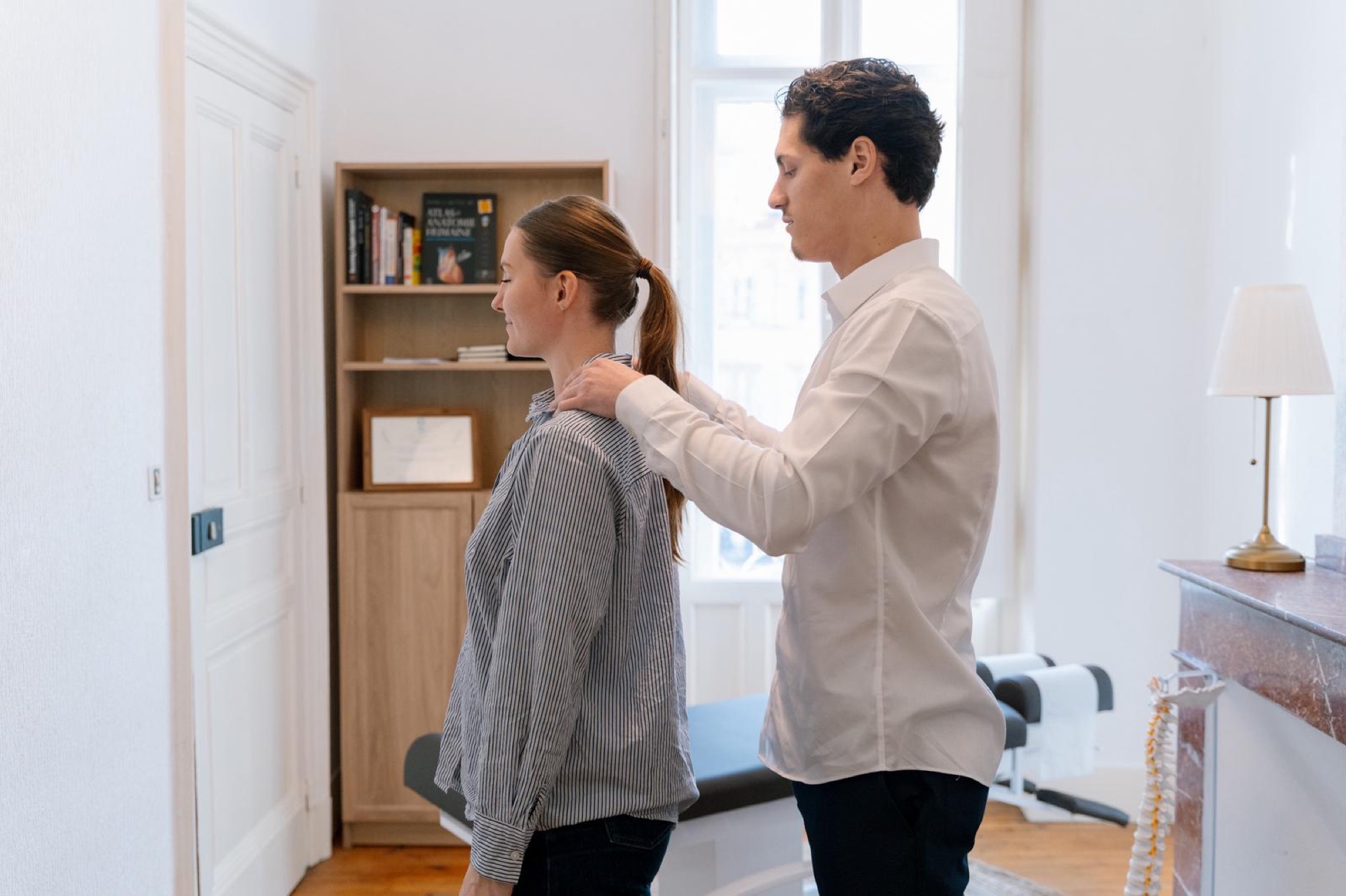 Thomas Nunes examine la posture d’une patiente debout, les mains posées sur ses épaules